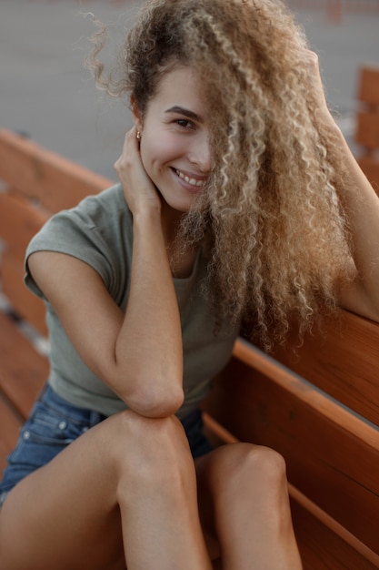 Divertente ritratto di una giovane e bella donna alla moda con i capelli ricci con un sorriso in abiti casual alla moda sulla strada