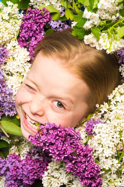 Divertente ritratto facciale di una bella bambina che fa l'occhiolino Ragazza adolescente con bouquet di lilla viola e bianco Faccina buffa Smorfia comica emozione divertente viso pazzo