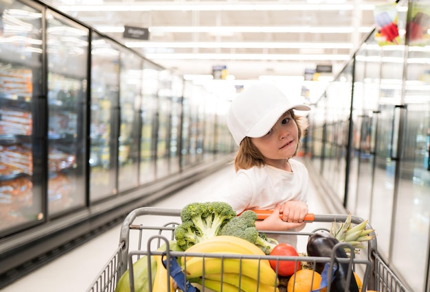 Divertente shopping gioioso bel bambino ragazzo in supermercato compra verdure cibo sano per bambino