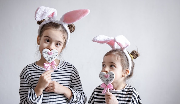 Divertenti bambine con orecchie di Pasqua in testa e pan di zenzero pasquale su bastoncini.