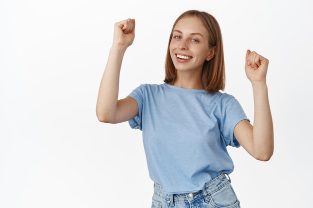 Divertiamoci un po'. Felice giovane donna che balla, ragazza che si gode la festa, alza le mani e festeggia, sorride spensierata, in piedi in t-shirt su sfondo bianco