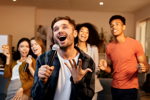 Divertimento a casa, bel ragazzo entusiasta e bello che canta con il microfono mentre gioca al karaoke con