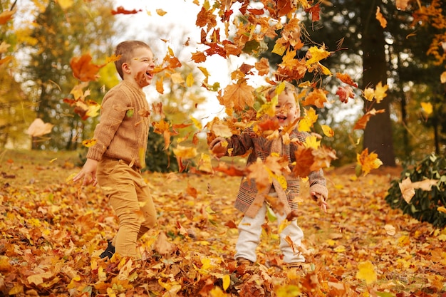 Divertimento all'aria aperta in autunno. Bambini che giocano con le foglie cadute autunnali nel parco. Piccoli amici felici.