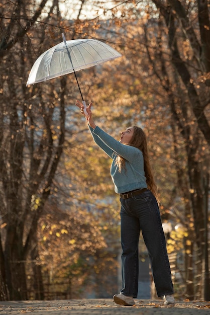 Divertimento bella giovane donna con ombrello trasparente Felice giovane donna con i capelli lunghi in autunno parco
