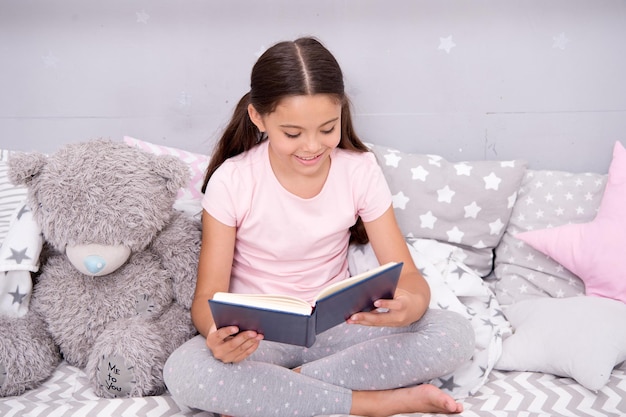 Divertimento di lettura prima di coricarsi. La ragazza felice ha letto il libro all'amico del giocattolo. Il bambino piccolo si diverte a leggere una storia di finzione. La lettura stimola il gioco di finzione. Sviluppare l'immaginazione. Leggere ti rende più creativo.
