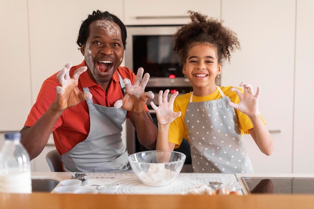 Divertimento in cucina Allegro padre e figlia neri che scherzano insieme mentre cuociono