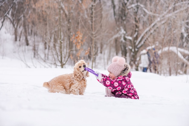 Divertimento invernale della ragazza del bambino in rosa e cocker spaniel