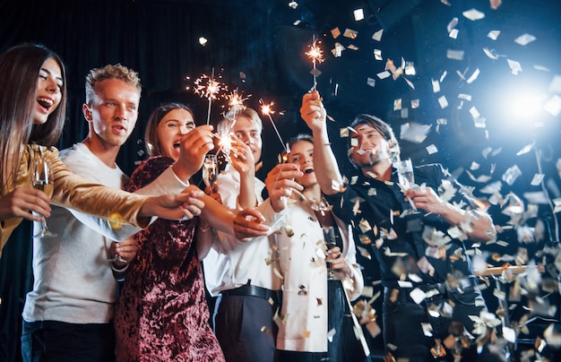 Divertirsi con le stelle filanti. I coriandoli sono nell'aria. Gruppo di amici allegri che festeggiano il nuovo anno in casa con un drink in mano.