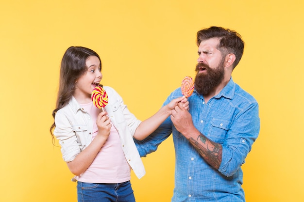 Divertirsi felice infanzia Figlia e papà mangiano caramelle l'uomo hipster con la barba è un buon padre bambina e papà tengono lecca-lecca colorate vibrazioni estive famiglia felice allegra per il negozio di caramelle da dessert