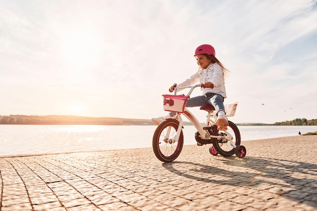 Divertirsi vicino al lago Bambina felice che guida una bicicletta all'aperto in estate