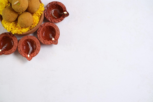 Diwali Rangoli usando Diya, fiori e Besan Laddu su sfondo bianco, fuoco selettivo