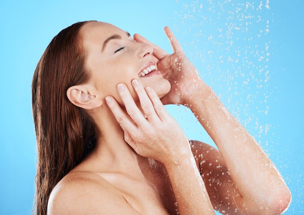 Doccia acqua e donna felice sorriso in studio sfondo blu e pulizia per l'igiene Giovane modello femminile che lava con gocce bagnate per la cura della pelle e la cura della pelle per la cura di sé benessere o routine