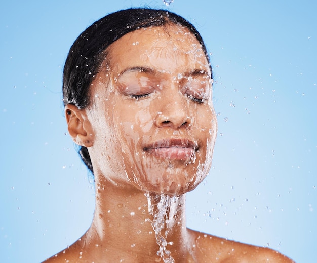 Doccia donna e spruzzi d'acqua sul viso per l'idratazione della cura della pelle o l'igiene pulita sullo sfondo blu dello studio Donna in lavaggio del viso con acqua per idratare o detergere per un trattamento igienico per la cura del corpo