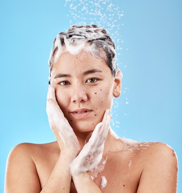 Doccia shampoo e donna per la cura dei capelli con sapone e ritratto pulito per la cura e l'igiene su sfondo blu dello studio Affrontare le mani e il benessere con il lavaggio dei capelli e la bellezza con gocce d'acqua