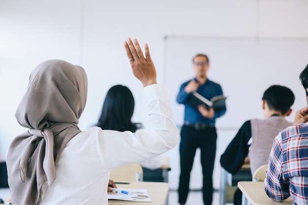 Docente che indica uno studente universitario con la mano alzata in classe Studente che alza la mano con un qu