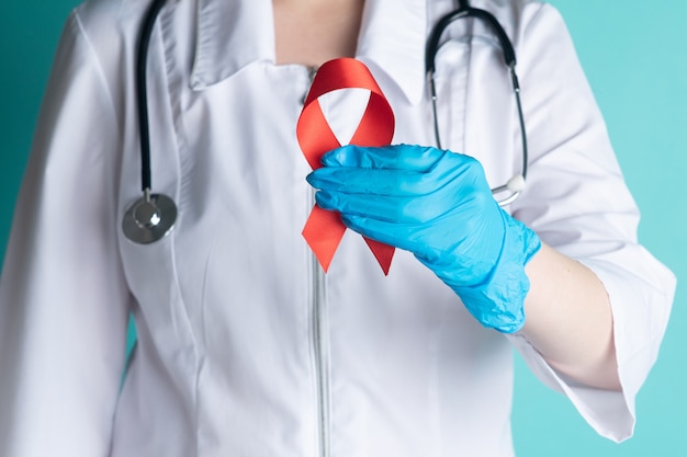 Doctor Hands tiene in mano Red Ribbon, AIDS, HIV International Symbol of Awareness, Healthcare and Medicine Concept. Primo piano della medicina femminile in uniforme da laboratorio che mostra il nastro per la cura dei simbolismi dell'HIV