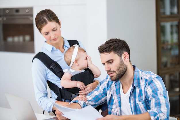 Documenti della lettura dell'uomo mentre moglie che trasporta bambino