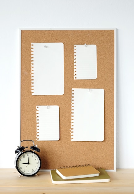 Documenti di nota in bianco sulla scheda e sull&#39;orologio del sughero sulla tabella di legno