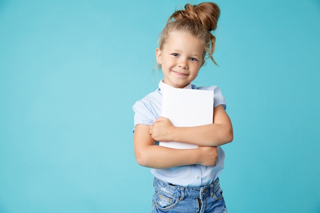 Dolce bambina felice in piedi con il libro isolato sopra la parete blu dello studio