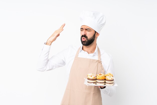 Dolce del muffin della tenuta del giovane sopra bianco isolato con l'espressione stanca e malata