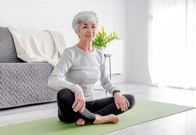 Dolce donna guarda in telecamera mentre si siede sul tappetino da yoga che incarna lo stile di vita attivo praticando a