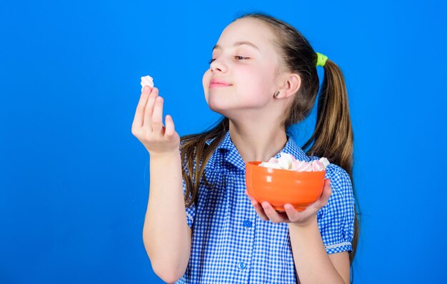 Dolce e morbido Concetto di dente dolce Calorie e dieta Ragazza faccia sorridente tenere ciotola dolci marshmallow in mano sfondo blu La ragazza del bambino con i capelli lunghi ama i dolci e le prelibatezze Chi se ne frega della dieta