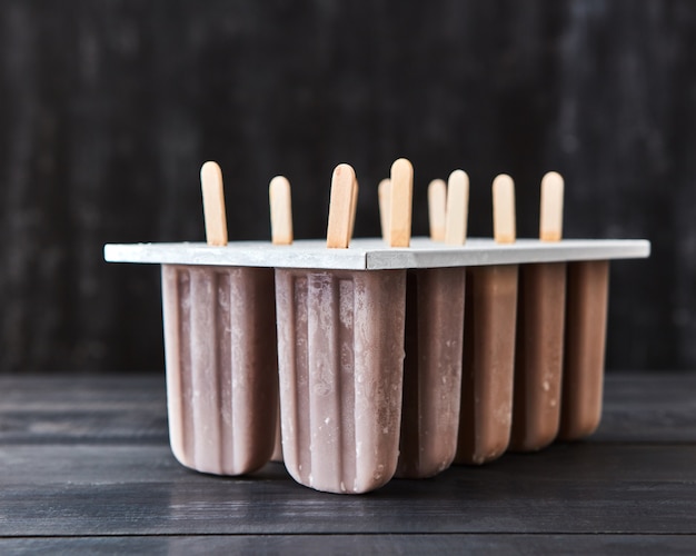 Dolce estivo freddo. Ghiacciolo di gelato al cioccolato fatto in casa su un bastone in uno stampo su un tavolo di legno scuro con una copia dello spazio per il testo.