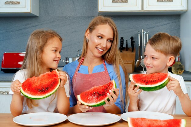 Dolce famiglia, madre e figli che mangiano anguria nella loro cucina divertendosi