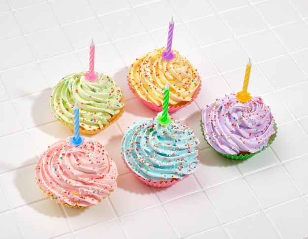 Dolce festeggiare multicolor crema cupcakes con candele in piedi su una superficie bianca Happy birthday concetto