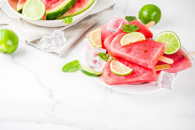 Dolce ghiacciolo di anguria e lime con anguria a fette e menta, su superficie di marmo bianco