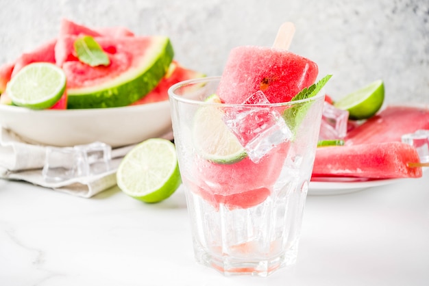 Dolce ghiacciolo di anguria e lime con anguria a fette e menta, sul tavolo di marmo bianco