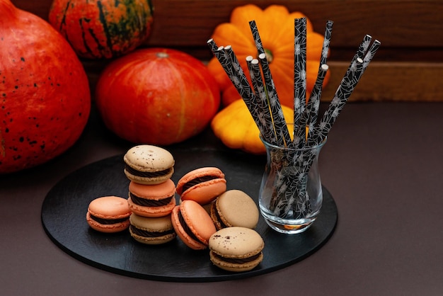 Dolce per Halloween. Menù del Ringraziamento. Macarons francesi. Amaretti al cioccolato su sfondo nero con zucche e cannucce da cocktail eco. Messa a fuoco selettiva morbida.