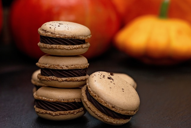 Dolce per Halloween. Menù del Ringraziamento. Macarons francesi. Amaretti al cioccolato su sfondo nero con zucche. Messa a fuoco selettiva morbida. Avvicinamento.