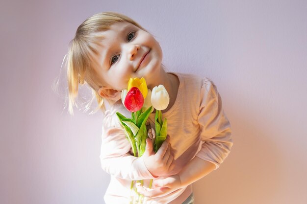 Dolce ragazza dai capelli bionda felice che tiene un mazzo di tulipani colorati nelle sue mani