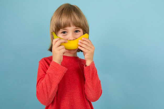 Dolce ragazzo europeo in maglione rosso con banana nelle mani in posa