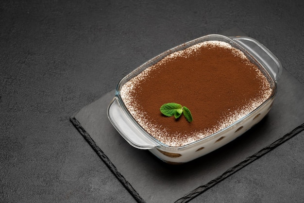 Dolce tiramisù italiano tradizionale in teglia di vetro sulla tavola di servizio di pietra su fondo o tavola concreti