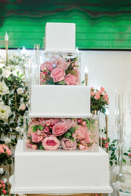 Dolce torta di fidanzamento bianca nella sala banchetti decorata con fiori artificiali e tante rose dietro