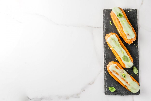 Dolce tradizionale francese. Mojito Eclairs con scorza di lime e foglie di menta, su blu scuro, vista superiore del copyspace