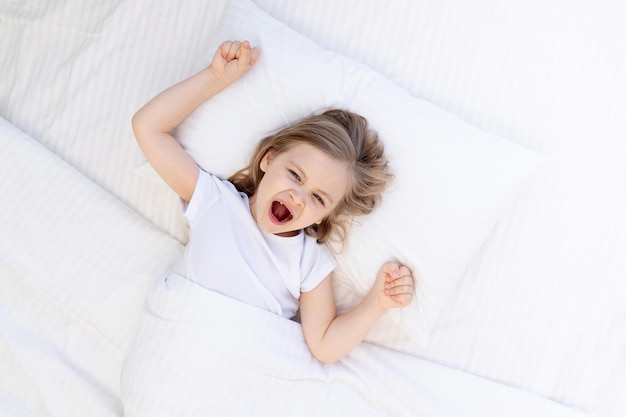 Dolcemente sbadigliante bambina che dorme su un letto su un cuscino di cotone bianco sotto una coperta il bambino sano dorme di notte