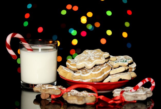 Dolcetti di Natale con un bicchiere di latte su sfondo di luci di Natale