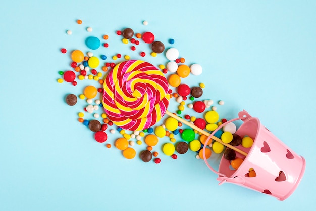 dolci al cioccolato colorati versati dal secchio con cuori su blu piatto laici