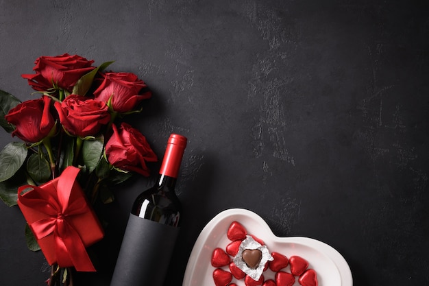 Dolci al cioccolato, rose rosse e vino rosso con regalo su nero per San Valentino. Biglietto di auguri con copia spazio.