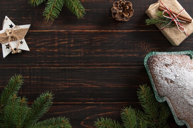 Dolci fatti in casa, biscotti a forma di albero di Natale, regali, rami di abete rosso e decorazioni su un tavolo di legno. Vista dall'alto.