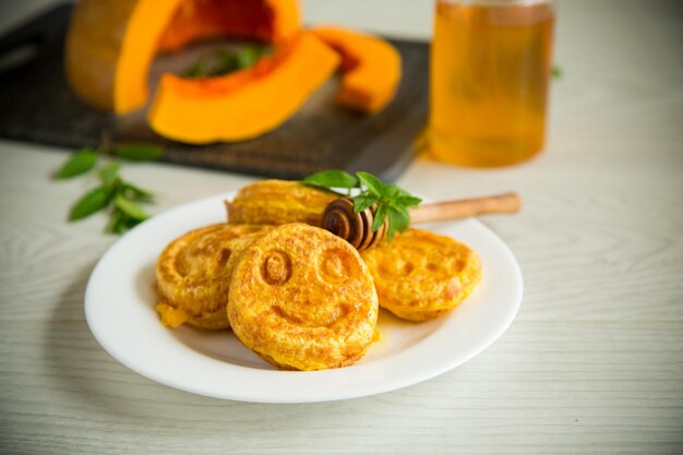 Dolci frittelle di zucca lussureggianti con miele in un piatto su un tavolo di legno