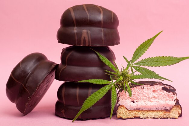 Dolci medici al cioccolato con THC. marshmallow al cioccolato e gemma di cannabis su uno sfondo rosa.