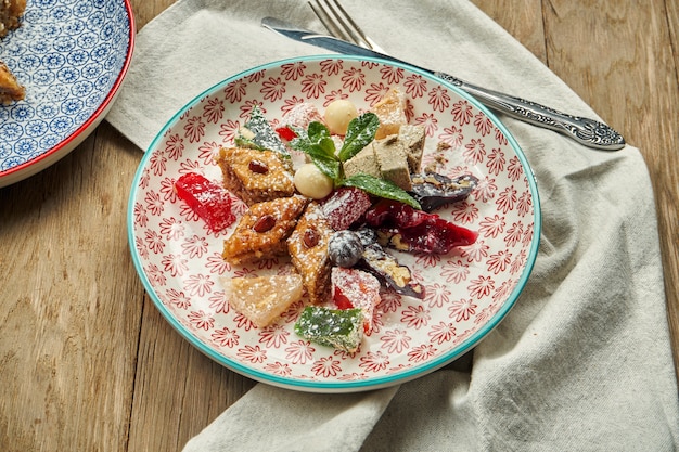 Dolci orientali classici - baklava con miele e noci, delizia turca, churchkhela in un piatto di ceramica rosso su un tavolo di legno