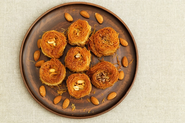 Dolci tradizionali del Medio Oriente "nido d'uccello" con miele e una varietà di ripieni di noci. Piatto piano delizioso del dessert marrone del miele. La vista dall'alto, copia spazio.