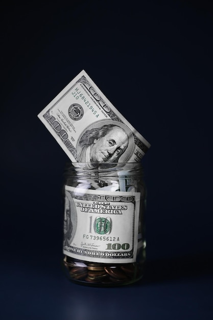 Dollari in un barattolo di vetro con monete su sfondo blu scuro. Concetto di risparmio di denaro