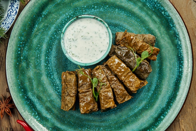 Dolma georgiano tradizionale - riso con carne tritata in foglie di vite su un piatto blu con salsa di yogurt. Superficie di legno. Vista dall'alto. Sarma