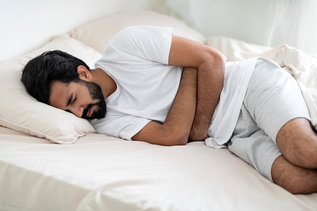Dolore addominale giovane uomo indiano che soffre di mal di stomaco mentre giace a letto